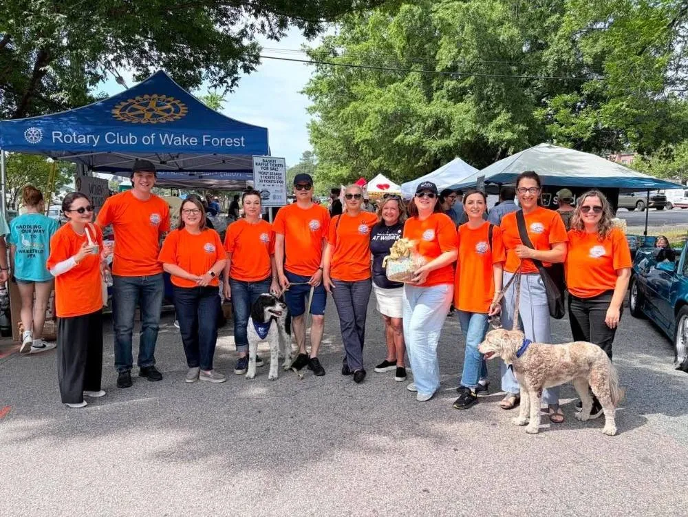 June 2026 delegates in orange volunteer shirts at the Rotary Club of Wake Forest tent, Cars and Carnivores Street Festival